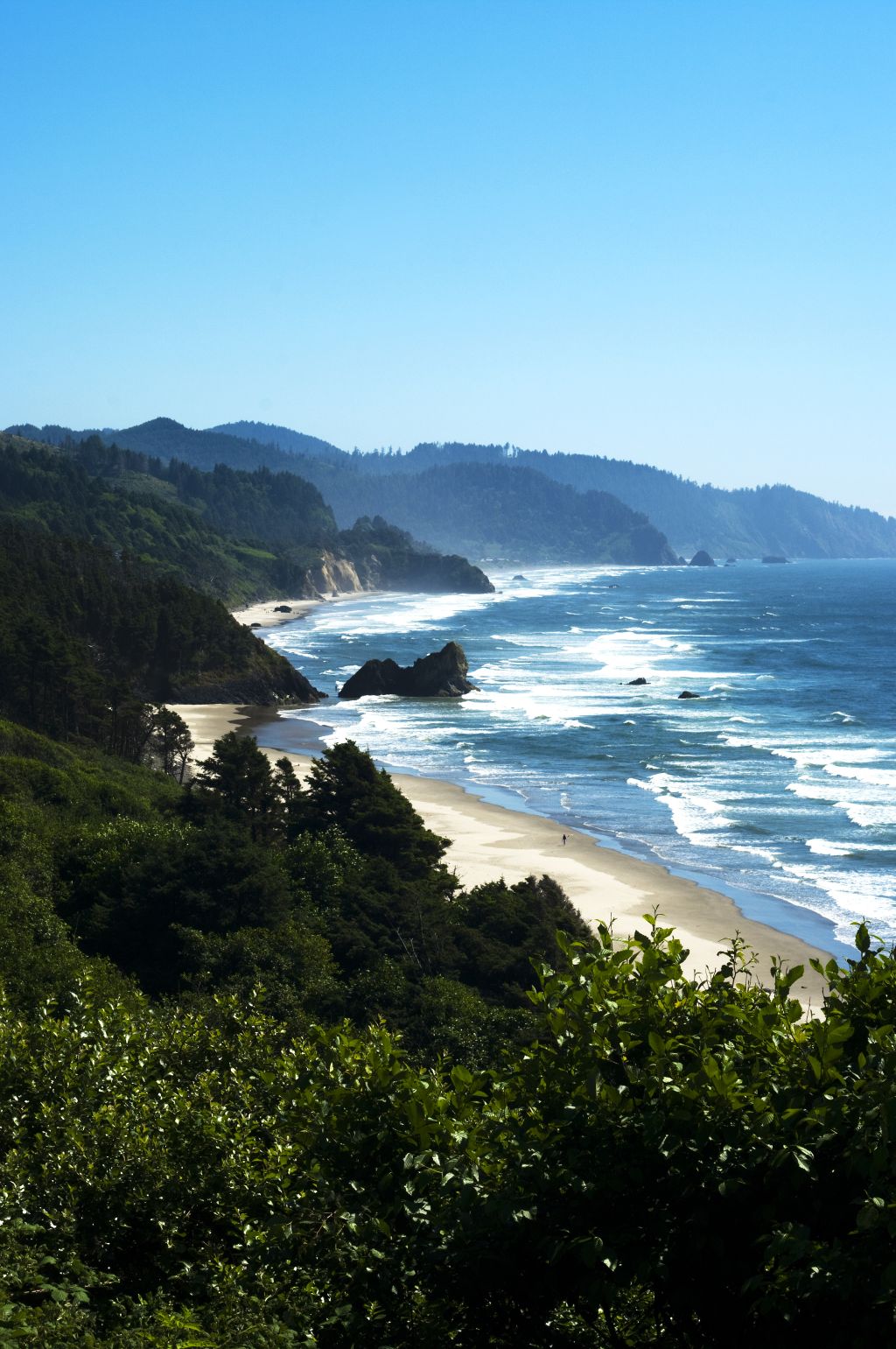 View from high above of green hills meeting sandy beach and crashing ocean waves below