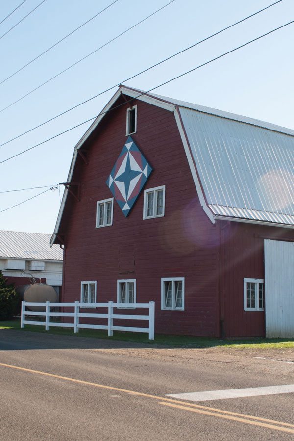 Exterior of red barn with a wooden quilt block facing the road