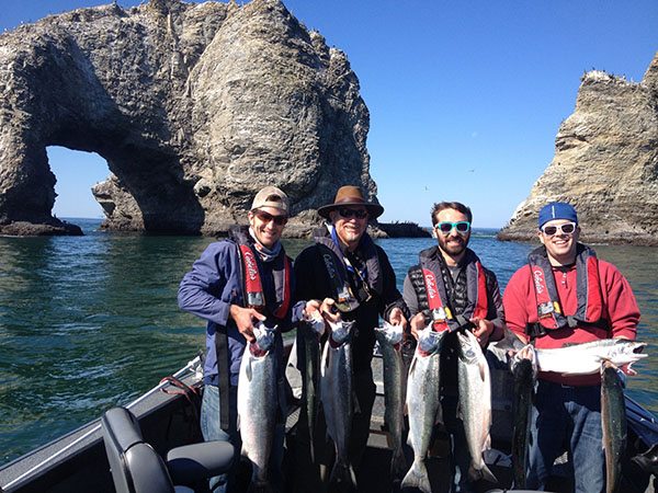 Four men stand on a boat, showing off the large fish they caught