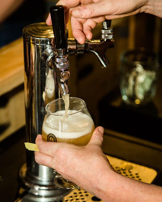 Closeup of hands pouring draft beer into a goblet-style glass