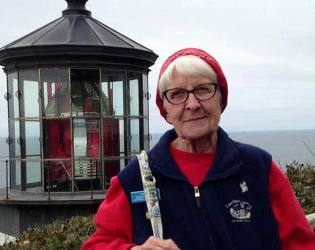 Oregon Coast Lighthouse keeper stands in front of lighthouse - woman wearing glasses and red hat