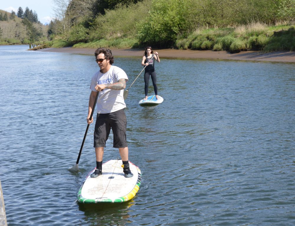 Two people on stand-up paddle boards with river bank in the background