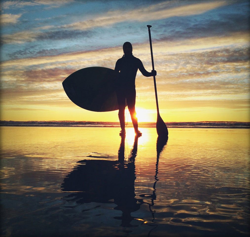 Silhouette of a person holding an oar and a paddle board in front of the sunset