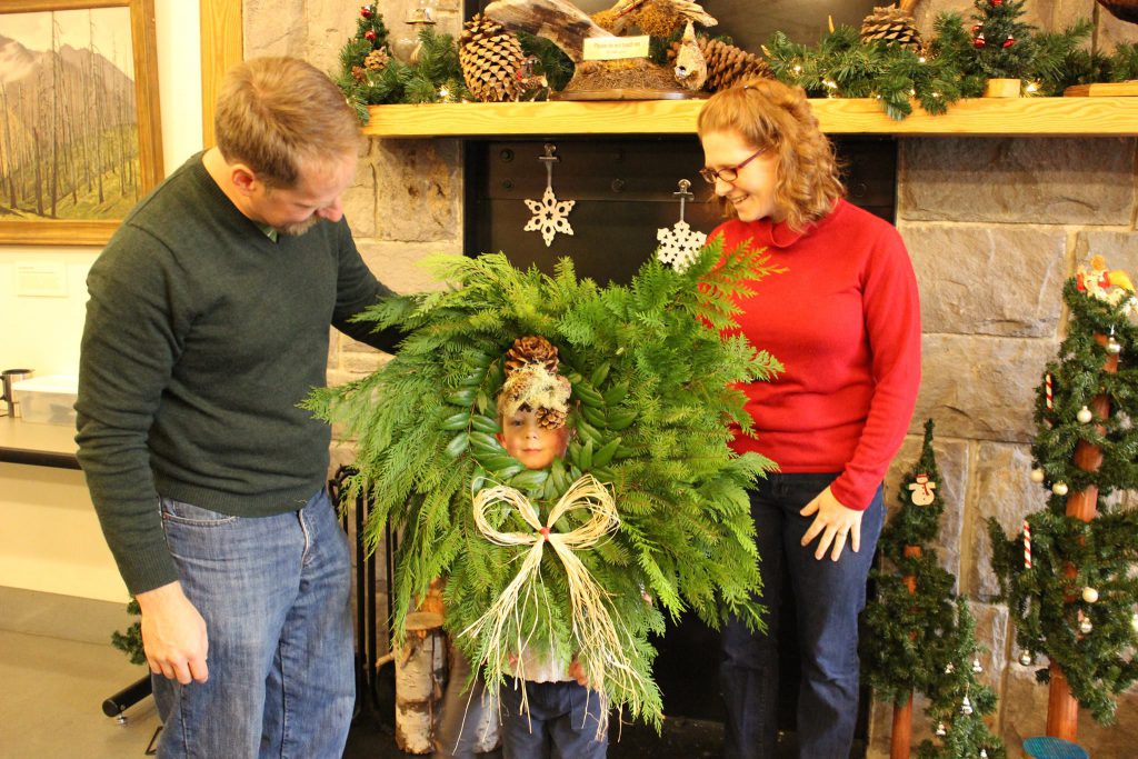 Man and woman stand around child with Christmas wreath around his head