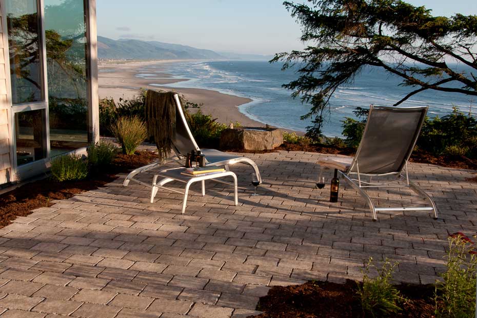 Paved patio area with lounge chairs and a bottle f wine, overlooking the beach