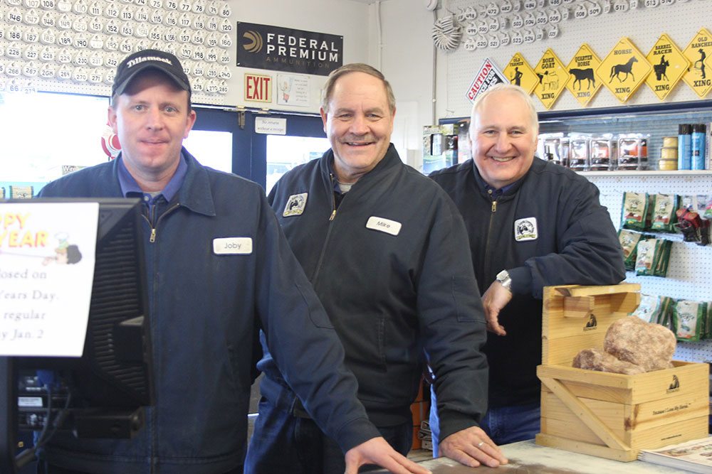 Three men in blue uniforms stand in the TCCA Farm Store
