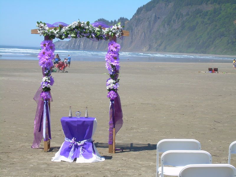 Wedding arch decorated with purple fabric and flowers on the beach