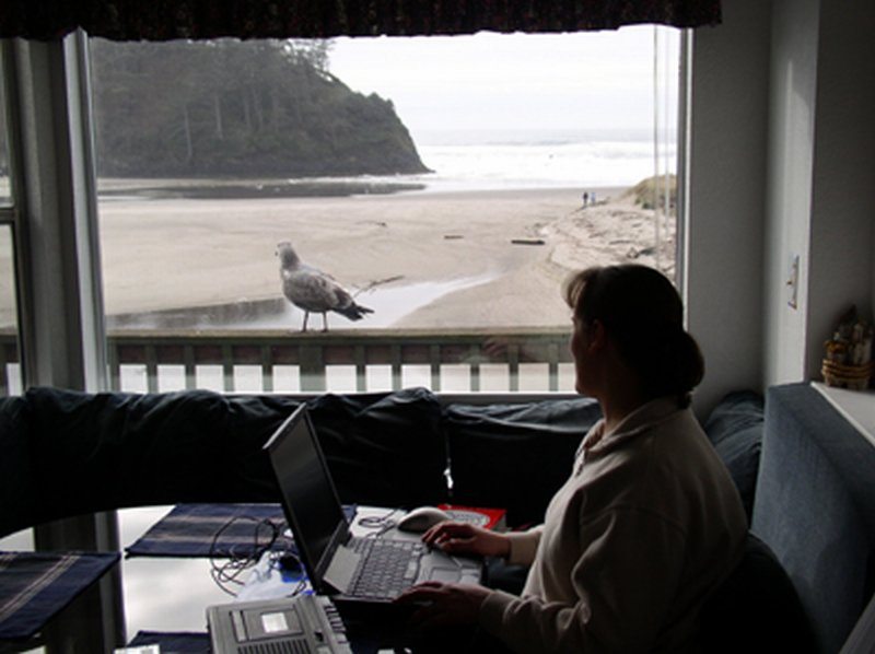 Woman working on laptop next to beachfront window