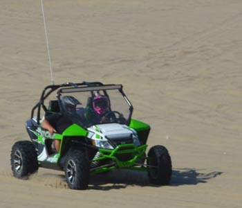 Two people sit in an ATV driving across sand dunes
